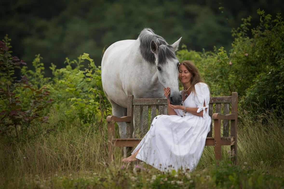 Elke-Wedig sitzt auf einer Holzbank und schmust mit ihrem Pferd